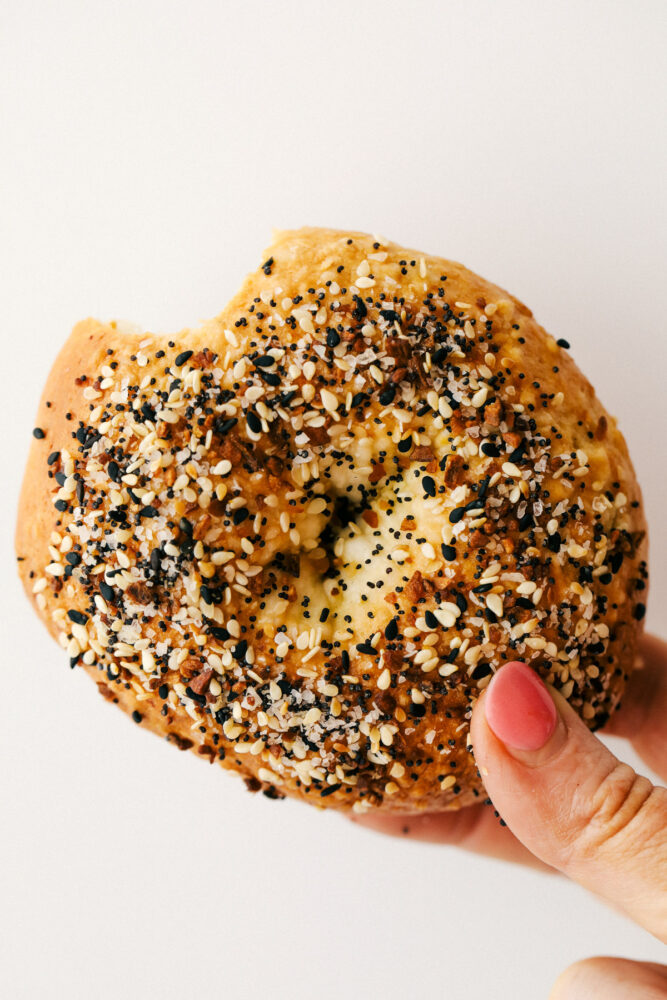 Holding a homemade seasoned bagel with a bite out of it. 