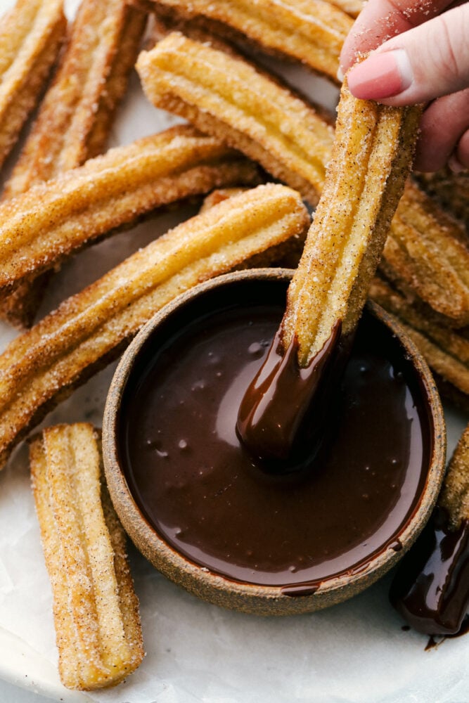 Holding a churro with chocolate sauce on it, with fired churros all around. 