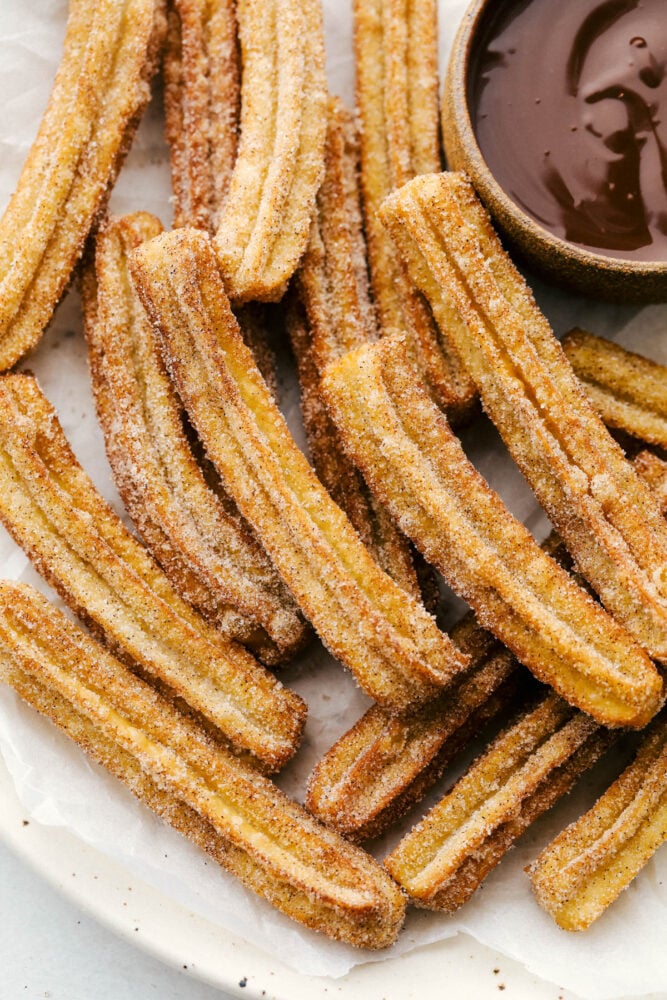 A pile of fried churros with a side of chocolate dipping sauce. 