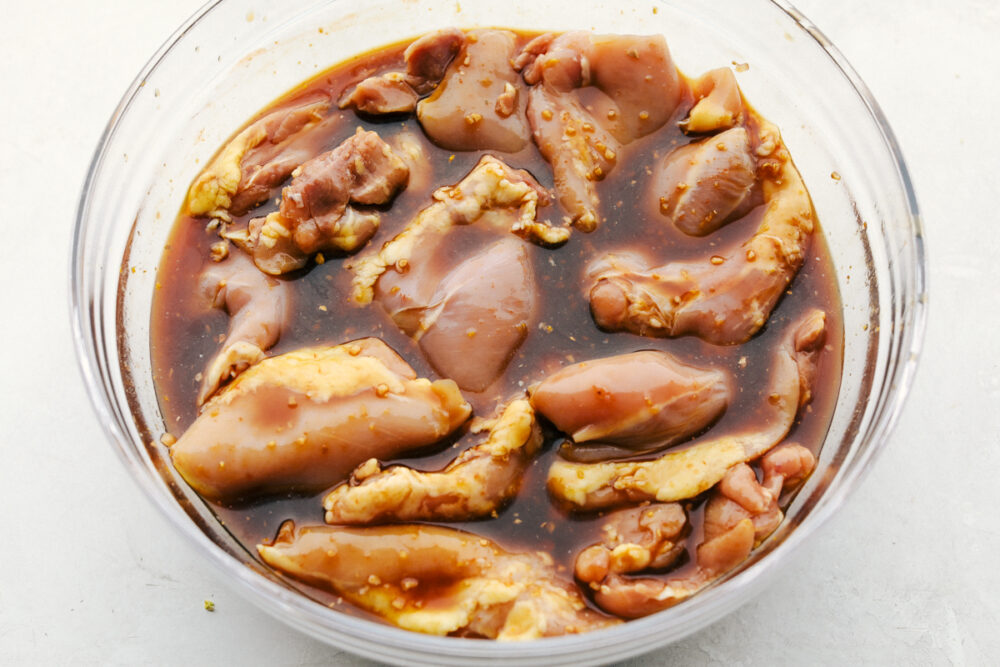 Chicken thighs sit in a bowl of marinade. 