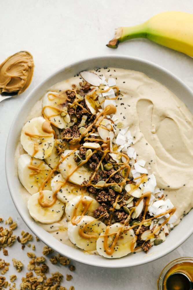 Peanut butter smoothie bowl, topped with bananas, chocolate granola and nuts. 