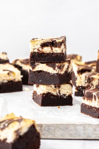 A stack of 3 cheesecake topped brownies on a white board.