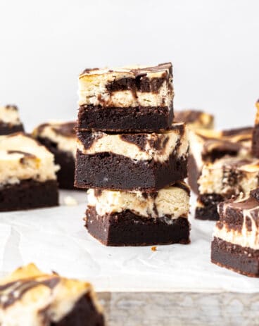 A stack of 3 cheesecake topped brownies on a white board.