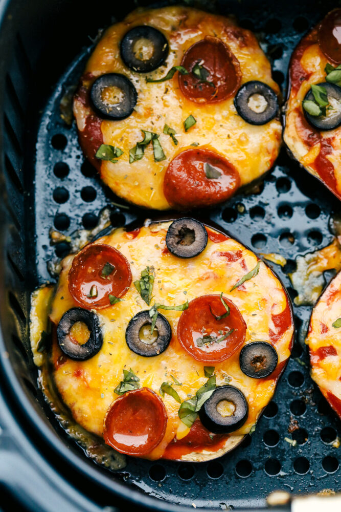 Cooked eggplant pizzas in air fryer basket.