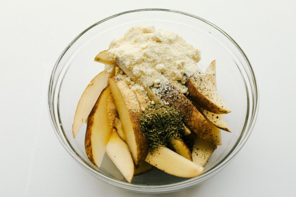 Potato wedges in a bowl with seasonings.