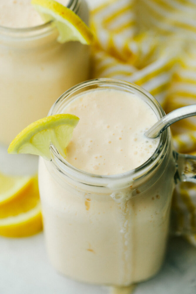 Creamy copycat frosted lemonade with a wedge of lemon and a straw. 
