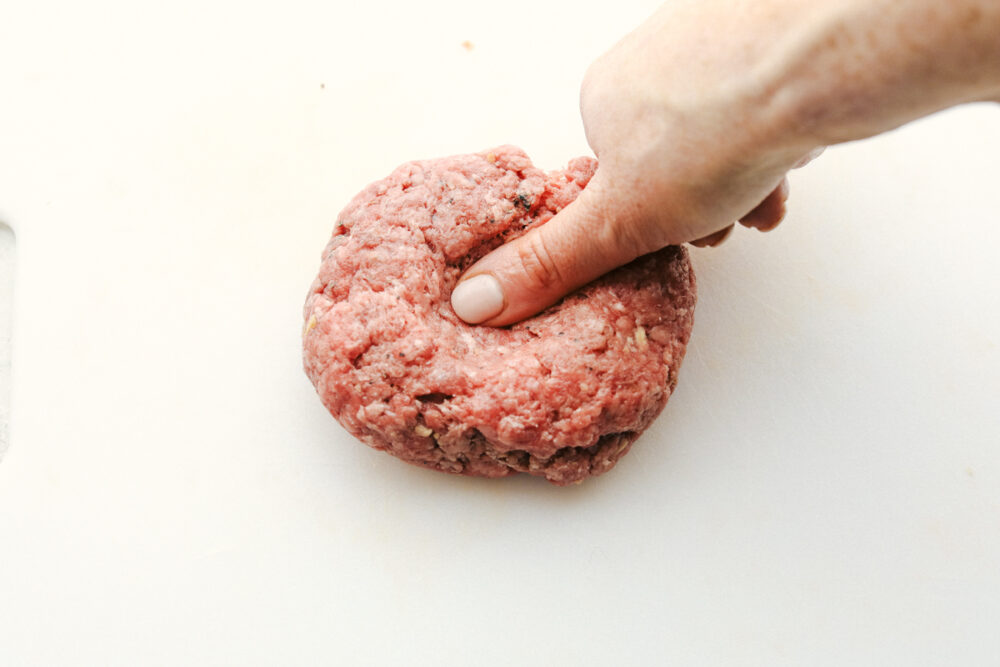 Putting a divot in the burger with a thumb. 