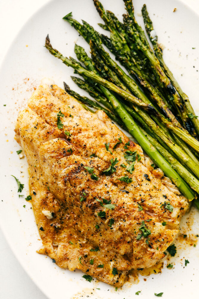 This Grilled Cajun Garlic Butter Cod is the only recipe you will need this summer! The cod is tender and juicy and the flavor is spicy and buttery, it's insanely delicious! Grilled Cod on a plate with grilled asparagus.