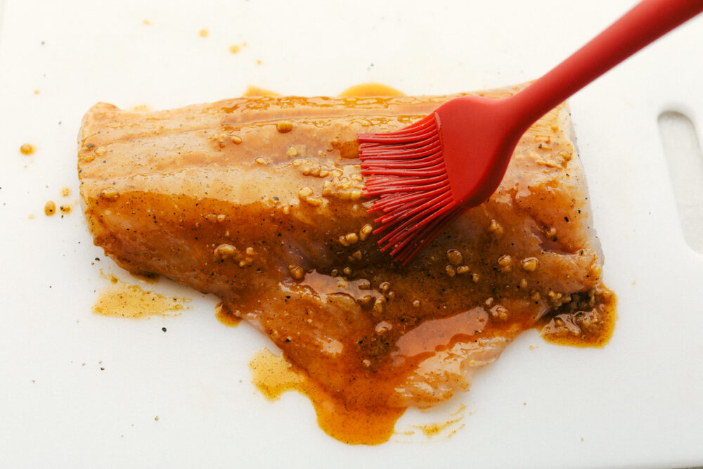 This Grilled Cajun Garlic Butter Cod is the only recipe you will need this summer! The cod is tender and juicy and the flavor is spicy and buttery, it's insanely delicious! Basting the cod with the cajun garlic seasoning.