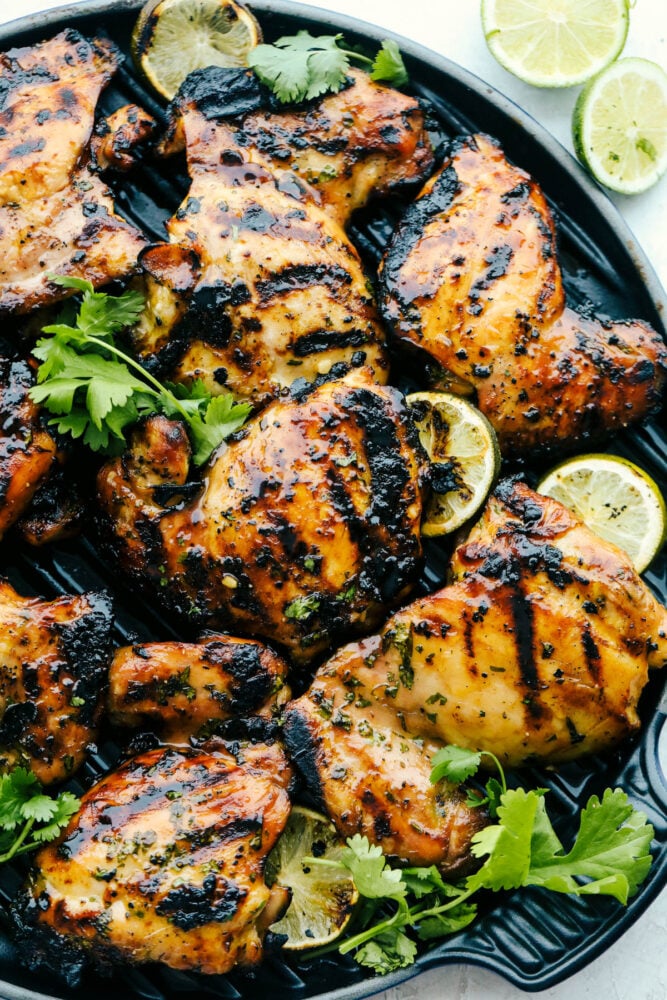Perfectly grilled tender and juicy chicken marinated in a honey lime cilantro marinade. The flavor of this chicken is incredible! A plate of grilled honey lime cilantro chicken garnished with cilantro and limes.