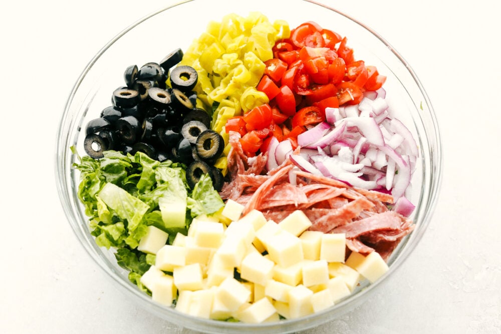 Ingredients for Italian chopped salad in a clear bowl, ready to be mixed. 