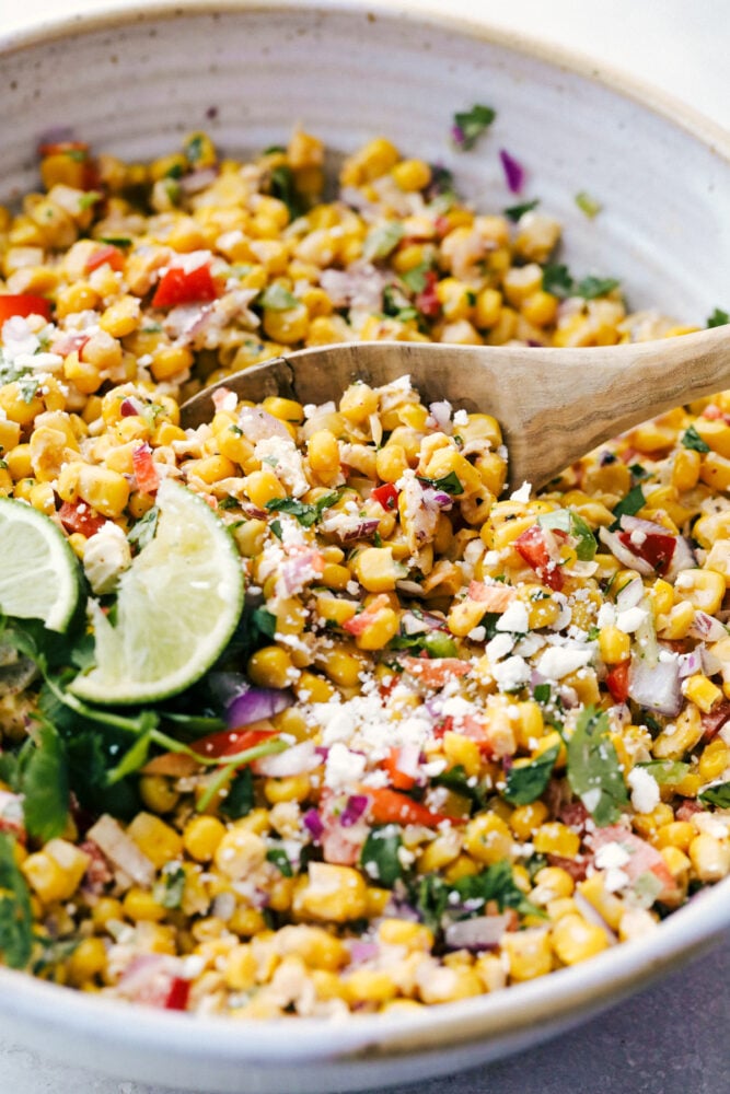 Stirring the salad together and serving it on a wooden spoon. 