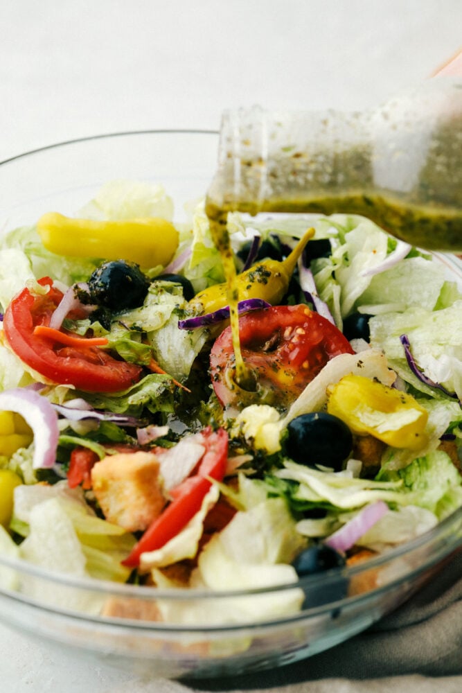 Pouring the olive garden salad dressing over a salad. 