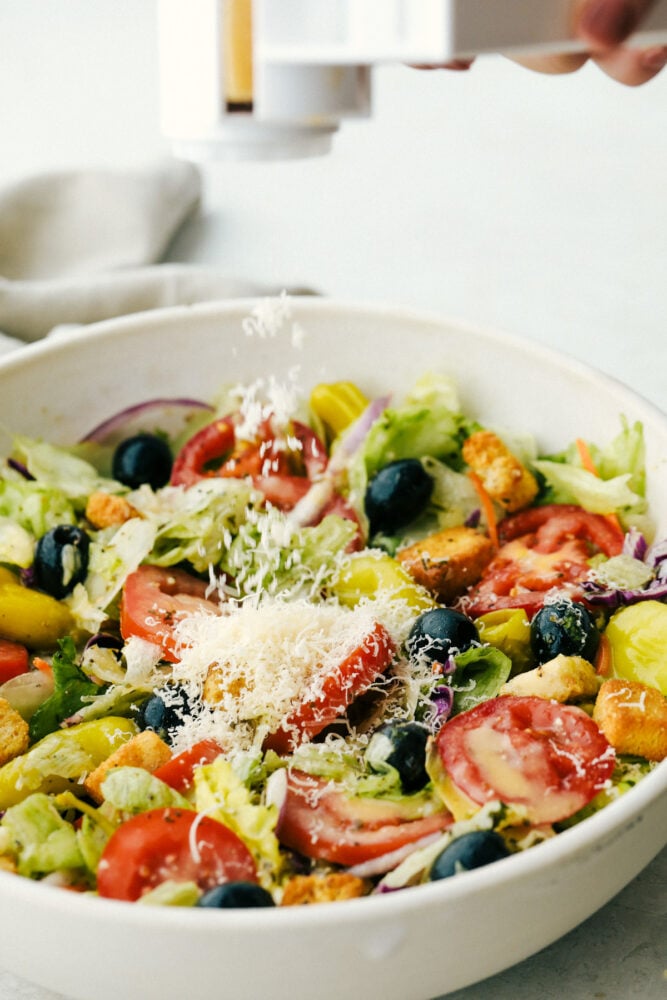 Copycat Olive Garden Salad is one of my all time favorite restaurant salads ever! And now you can have this bright zingy incredible salad at home! Adding Cheese to a bowl of salad.