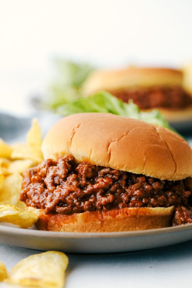 A sloppy joe on a plate with potato chips. 