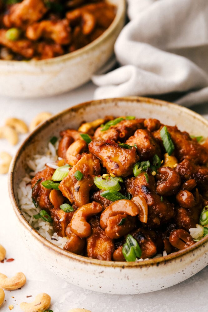 A bowl of cashew chicken on top of a bed of rice. 