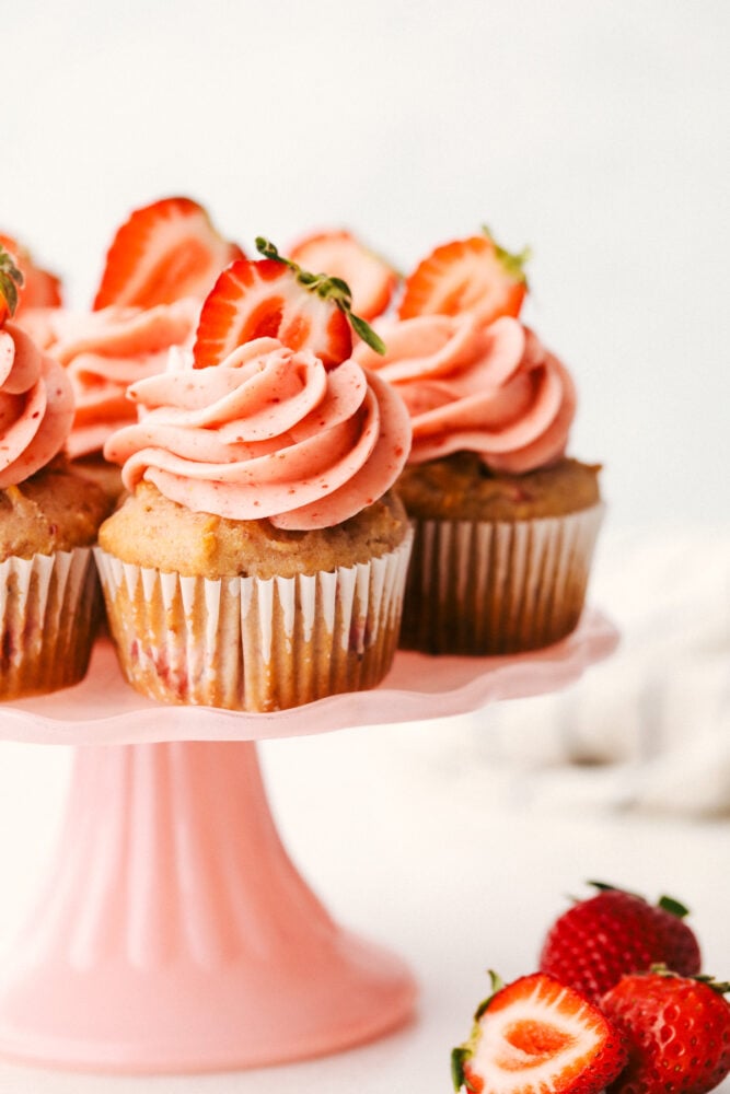 Strawberry cupcakes on a platter with frosting and strawberries on top.