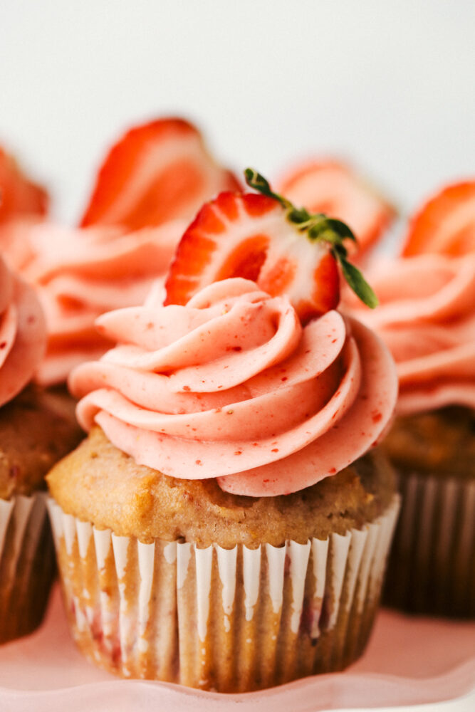 A strawberry cupcake with swirled frosting and a strawberry on top.