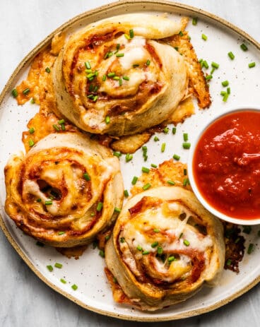 A white plate with pizza pinwheels and a red dipping sauce.