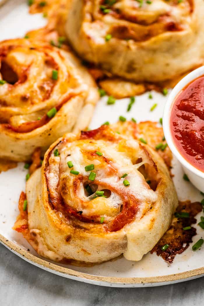 A closeup of pizza pinwheels on a plate with dipping sauce. 
