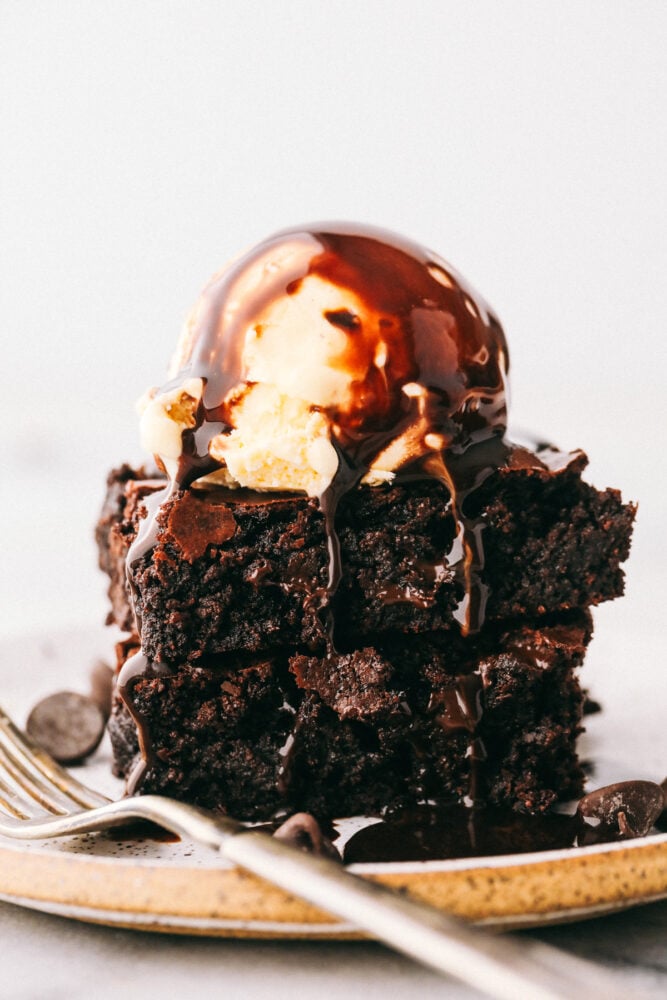 Two brownies with ice cream and chocolate sauce dripping down the sides. 