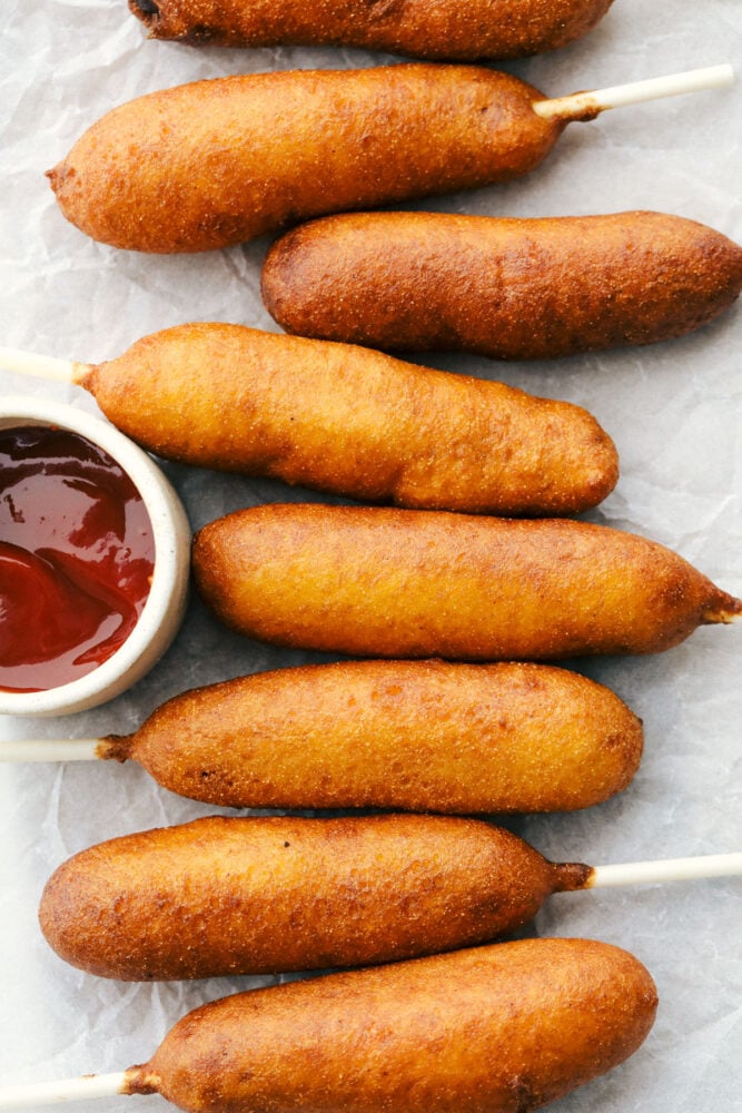 Corn dogs lined up ready to eat with a side of ketchup.