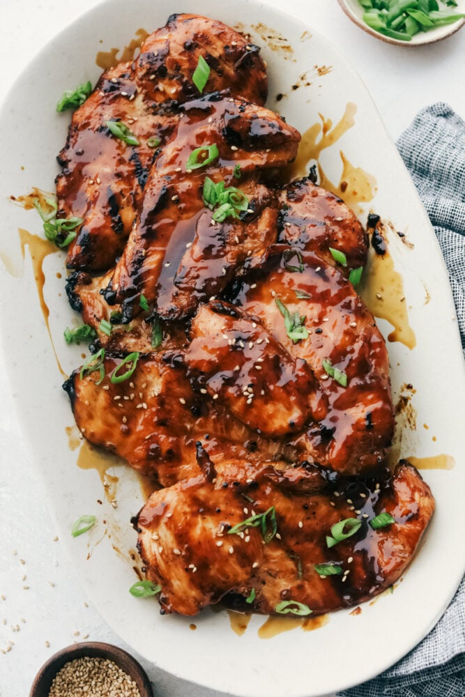Grilled teriyaki chicken breasts on a platter garnished with green onions and sesame seeds. 