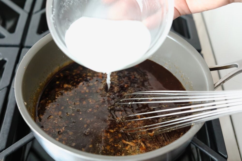 Adding the cornstarch slurry to thicken the sauce. 