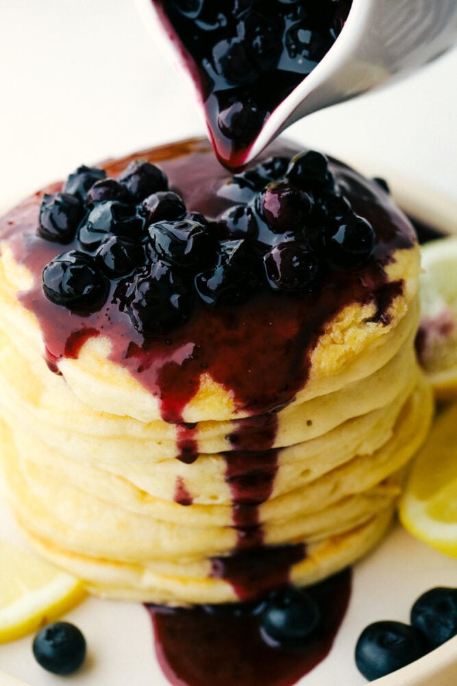 Blueberry sauce drips down a stack of ricotta pancakes. 