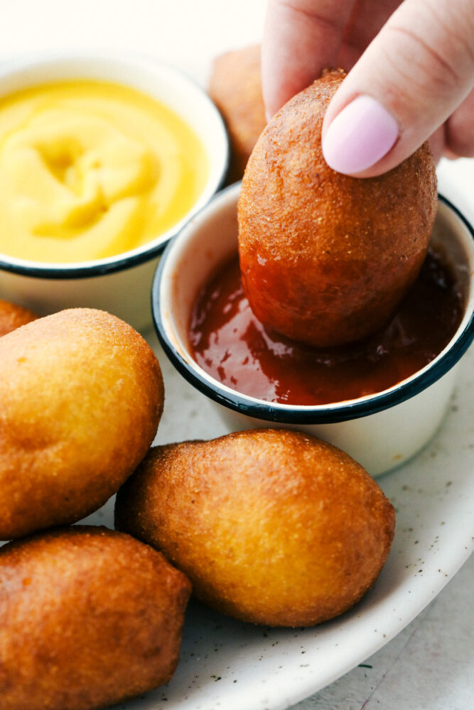 Mini corn dogs being dipped in ketchup. 
