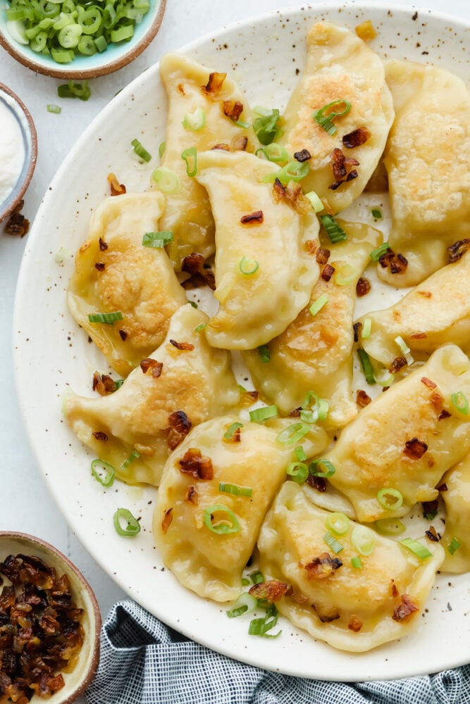 A plate of cooked pierogi garnished with green onions. 
