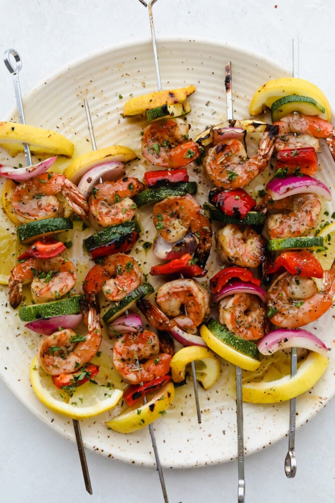 Shrimp Kabobs are marinated and grilled to perfection for the most scrumptious summer meal. Full of zesty flavors the whole family is going to love these kabobs! Shrimp and vegetable skewers grilled and on a plate ready to eat.
