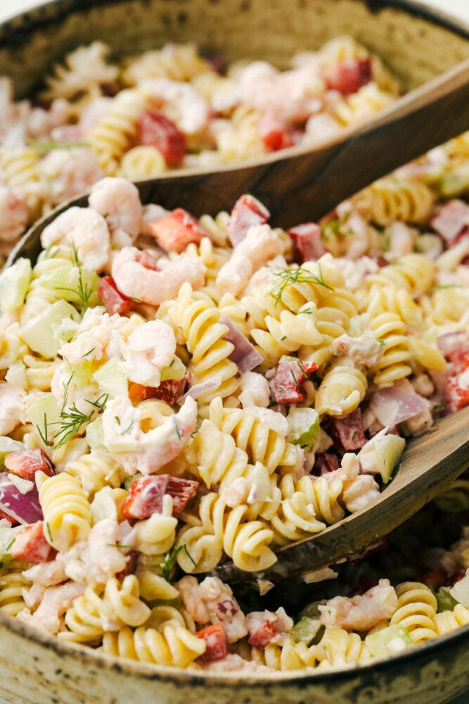 Up close photo with shrimp pasta salad and two wooden spoons in the salad. 