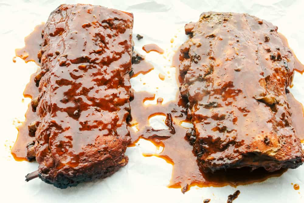 Cooked ribs on a baking sheet with sauce from crockpot poured over the top.