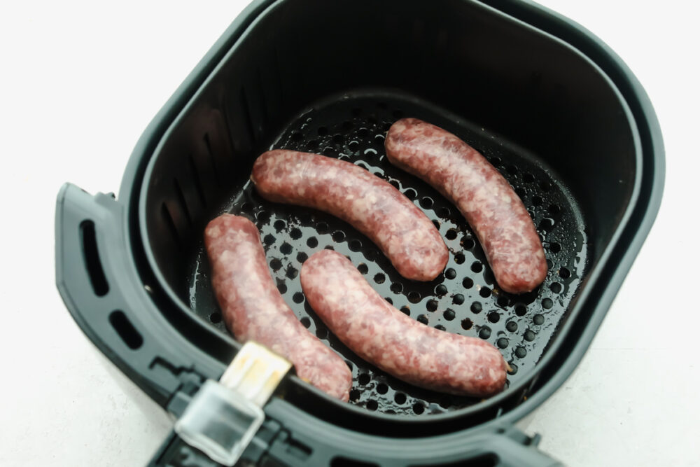 Air frying Brats is the best way to get a perfectly cooked brat and super easy!! The best part about these is you can have them year-round with an Air Fryer! Brats in the air fryer basket ready to cook.
