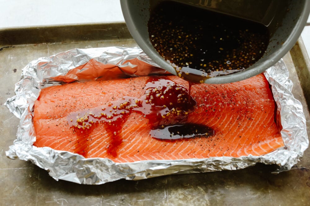 Pouring glaze over salmon in tin foil.
