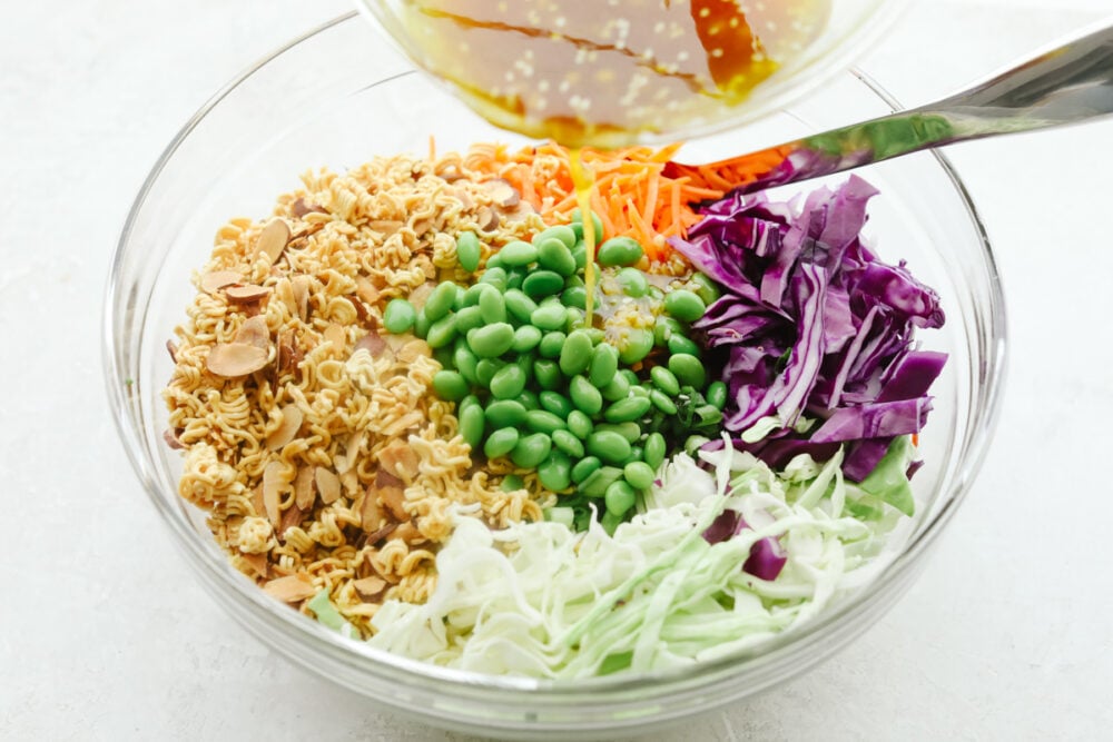 Pouring the dressing over the ingredients for Asian ramen salad.