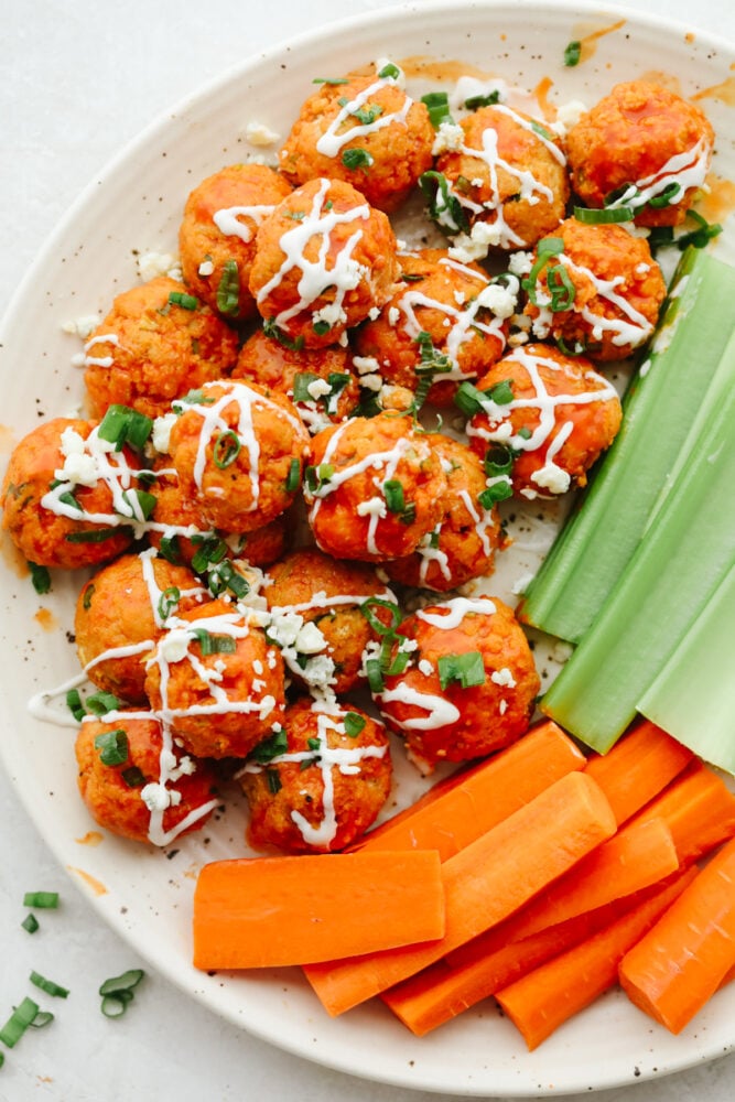 Buffalo chicken meatballs on a white plate with celery sticks. 