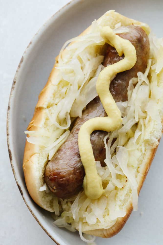 A cooked Brat in a bun with sauerkraut and mustard. 