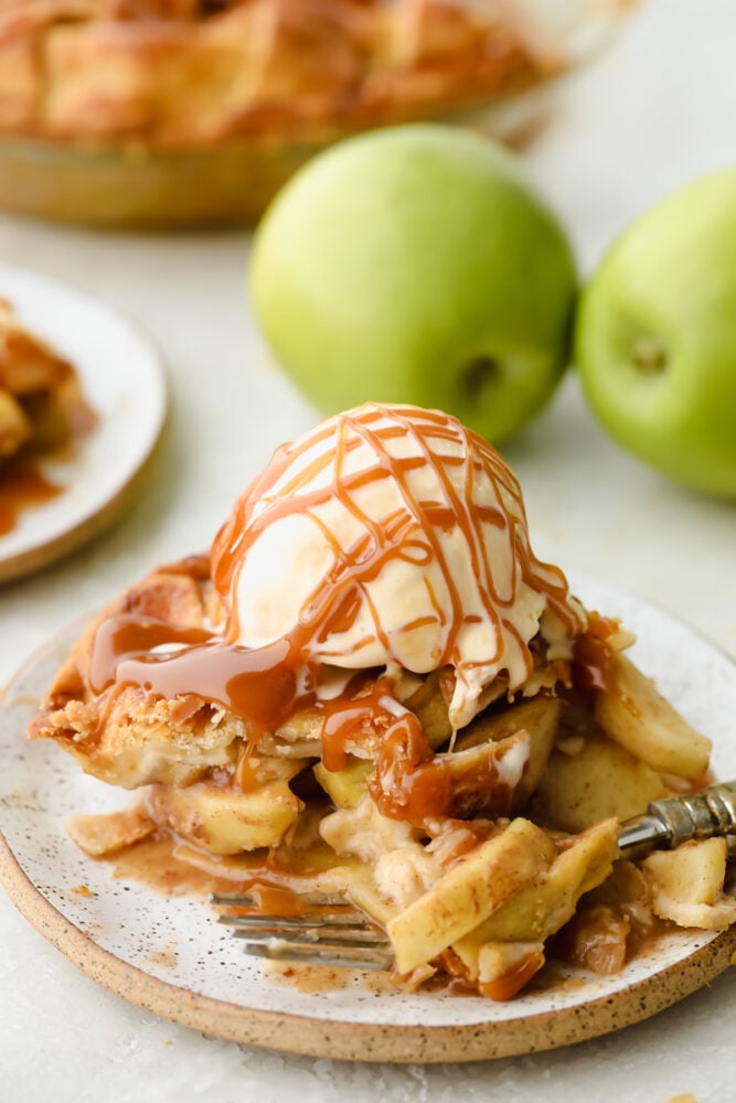 A slice of caramel apple pie with ice cream and caramel drizzled on top. 