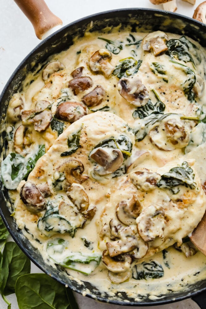 Scooping the chicken in the pan with the sauce and mushrooms and spinach. 