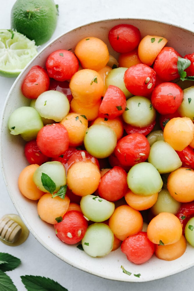 A bowl filled with different types of melons topped with a dressing.