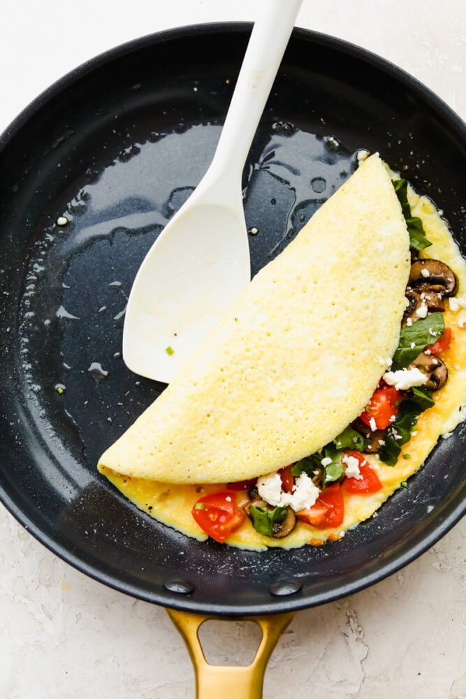 Omelette in a skillet filled with ingredients folded in half.