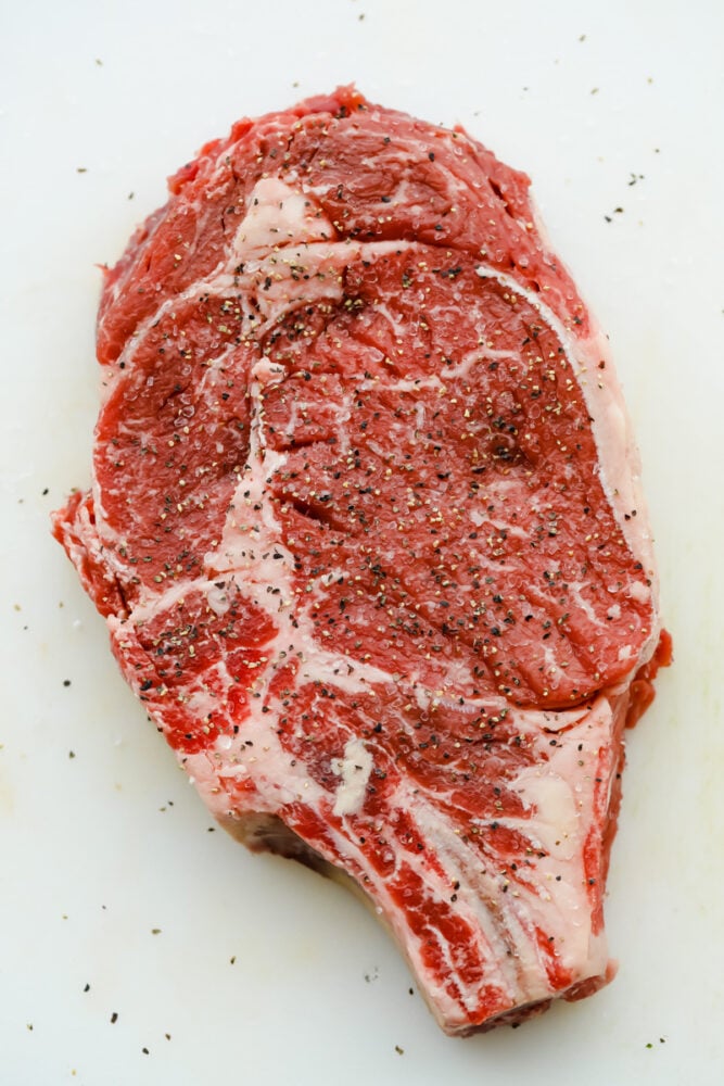 A raw ribeye steak salted and peppered.
