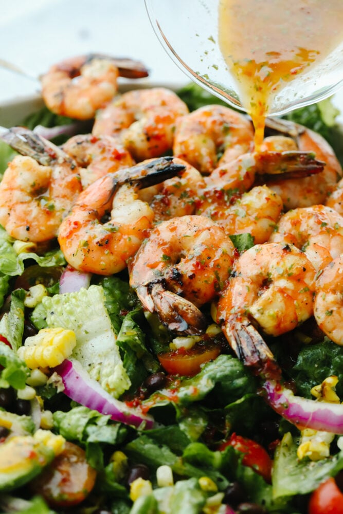 Pouring dressing over greens and grilled shrimp.