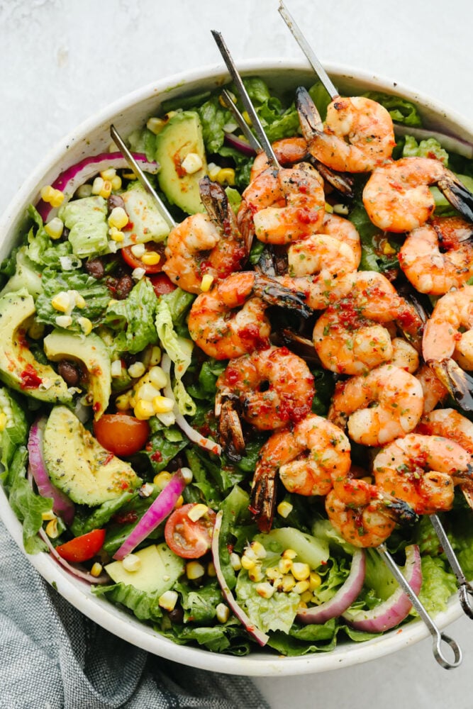 Greens in a white bowl topped with grilled shrimp.