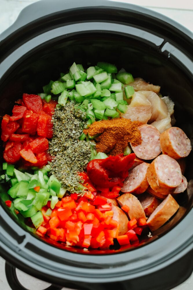 Vegetables, spices, chicken, and sausage in a slow cooker.