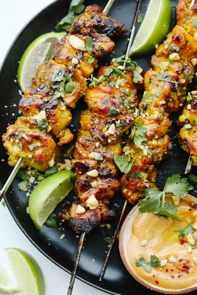 Thai Chicken skewers on a plate garnished with cilantro and peanuts. 