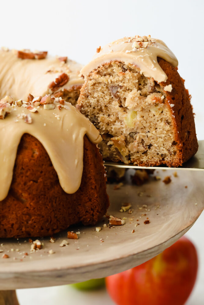 Praline apple bundt cake on a cake stand being sliced with a knife. 