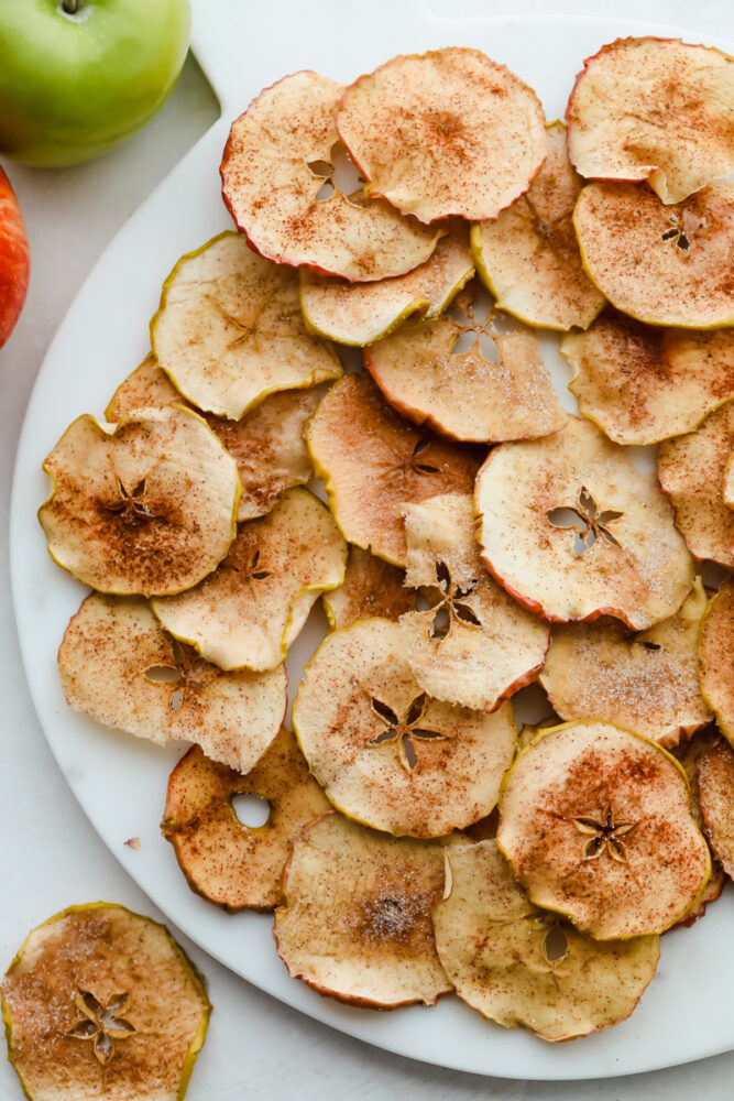 Baked Cinnamon Sugar Apple Chips is a healthy crunchy snack that is going to impress! Crunchy, crispy, sweet, and a bit spicy, these are going to change snack time Crisp baked cinnamon sugar apple chips on a white plate.